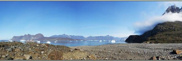 Panorama vu du haut de la balade, au loin, au pied de la falaise, un petit bateau de pêche est à l'ancre - Karrat Fjord - Groenland